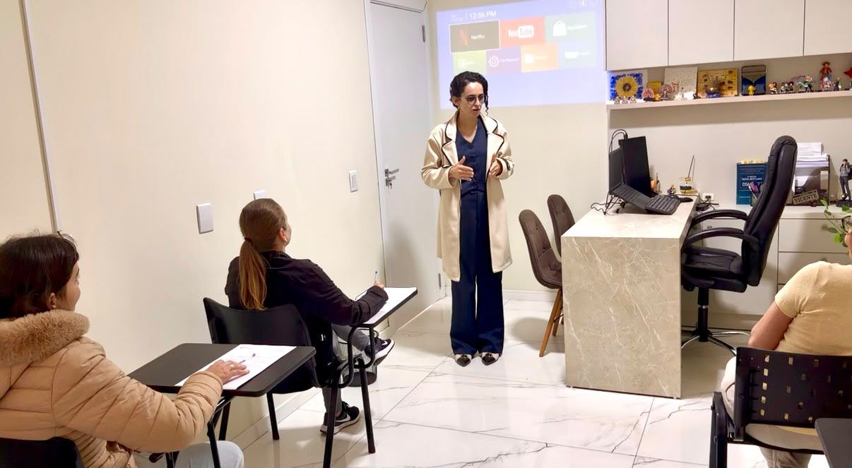 Aline Vicente, de pé, conduzindo uma aplicação coletiva de testes na clínica (participantes ilustrativos)